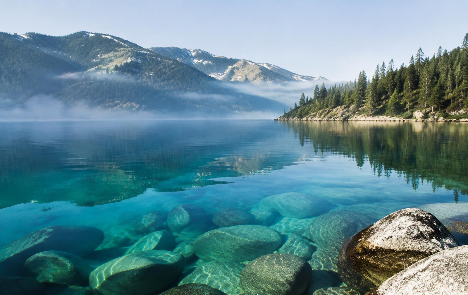 Clear alpine lake with granite stones and pine-covered mountains